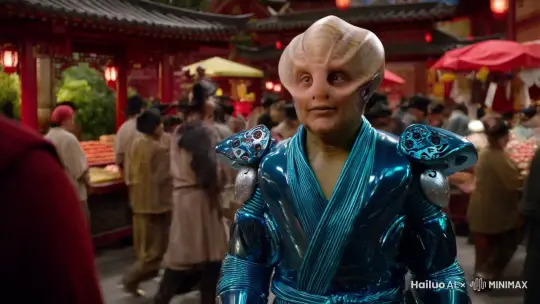 电影镜头，外星人角色活泼幽默，身穿高科技赛博道袍，面对镜头眨眼和挥手，背景中式古典市场中各种奇异角色来来往往。 by Hailuo AI Video Generator