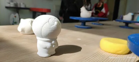 图中的哆啦a梦石膏缓缓走向屏幕前方，身体逐渐变为正常的蓝白色，铃铛是黄色。在全身变色之后他变得栩栩如生，从他的口袋中掏出了写着上岸的纸条。 by Hailuo AI Video Generator