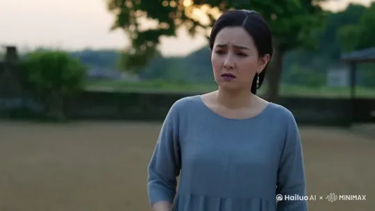 主要提示词：
温婉女子，35岁，蓝灰色素服，忧虑表情，眉头轻锁，双手纠结，站姿犹豫不决，目光游移。

表情细节：
- 眉心微皱
- 嘴唇微抿
- 目光低垂
- 面露难色
- 时而抬头看向远方

姿态描述：
- 双手交握胸前
- 身体重心轻微摇摆
- 脚步微微踌躇
- 肩膀略显紧张
- 偶尔深呼吸

画面氛围：
- 院落环境
- 暮色柔光
- 远处若隐若现的城郊 by Hailuo AI Video Generator