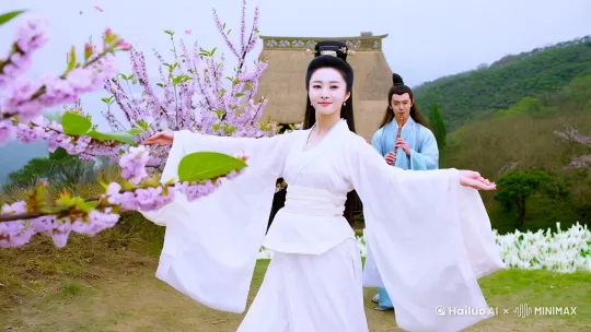 在一个高山山顶，一个东方面孔女人穿着中国白色古装在梅花丛里翩翩漫舞[推进]， 樱花瓣随风飘摇。可以看到是脸上洋溢着幸福的谈谈满足的微笑，缓缓抬头看向旁边俊美的男子。[右摇]旁边10米开远站着一个身穿浅蓝色飘逸古装，长相俊美的长发束发年轻男子吹着玉笛。温柔的看向跳舞的女子。男子的裙摆随分飘动。[变焦拉远]他们身后是一处茅草屋，屋子周围种满了铃兰。画面色调自然和谐。 by Hailuo AI Video Generator
