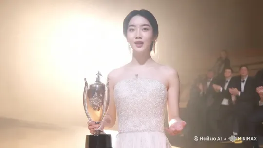 舞台上，聚光灯下，该角色穿着晚礼服拿着奖杯，自信的致辞。观众热情的鼓掌 by Hailuo AI Video Generator