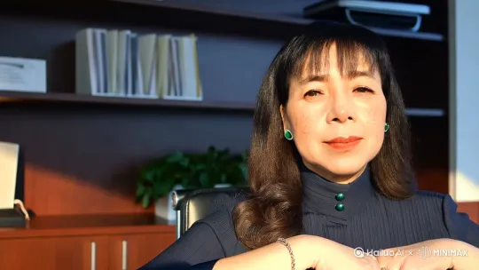 【中青年女性形象设计】
年龄区间：38-45岁坐在办公椅上
整体风格：优雅知性中透出岁月沉淀的从容感
 

 
- 脸型：鹅蛋脸线条柔和，下颌角有轻微棱角感
 
- 眉骨：立体但不过分突兀，挑眉弧度自然
 
- 眼型：杏仁眼尾微微上挑，虹膜呈琥珀金棕色
 
- 睫毛：自然卷翘不夸张，下睫毛根根分明
 
鼻梁直且挺，鼻尖微翘带点俏皮感
 
M型唇峰明显，下唇丰润，日常涂豆沙色口红
 
皮肤光泽感底妆下透出健康血色，两颊有淡褐色日晒斑
锁骨位置的中长卷发，发尾向内扣
 
自然分界的偏分刘海修饰发际线
 
发色是深亚麻棕，阳光下泛出暖金色

 手腕戴着细链镯
 
耳朵戴着祖母绿耳钉 by Hailuo AI Video Generator