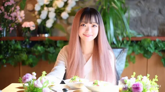 一个穿着裙子的20岁可爱女人坐在餐厅里面，头发是淡淡的粉色，发型是长发加齐刘海，全程只是面带微笑，不说任何话，先朝着镜头温柔挥手，然后站起身双手展开做出要拥抱的动作，餐厅的装修风格是小清新，墙上有绿植和花朵，女人的餐桌上也有淡雅色的花束放着，还有两个日式料理 by Hailuo AI Video Generator