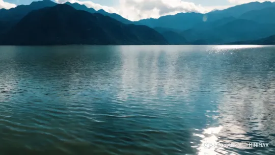 镜头快速跟踪，无人机航拍，远景俯瞰波光粼粼的湖面，以层叠山峦与低垂云霭构建空间纵深。一个300斤的大妈如离弦之箭飞速踏水疾驰，双足站立轻触水面形成连贯的轻微的水花，长长的水痕如银龙般蜿蜒身后。采用动态追踪镜头全程锁定人物，在保持远景视野的同时通过轻微环绕晃动增强速度张力。画面强化水面反光与阳光折射，使飞溅的水珠呈现钻石般璀璨光斑，衣摆翻飞的残影与水痕拖曳的轨迹形成动态呼应。以高帧率捕捉足部入水瞬间的涟漪扩散，搭配电影级冷色调强化冷冽质感，最终通过疾行速度与水痕延展的视觉对比，打造极具东方武侠意境的水上轻功奇观。 by Hailuo AI Video Generator