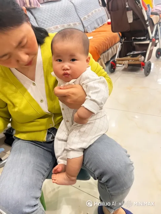 画面主体是图中穿着白色格子连体衣的宝宝,场景设定为在妈妈腿上,随后宝宝自行从妈妈腿上走下来到地面。要展现宝宝自然的走路姿态,动作流畅不僵硬,表情生动,环境光线与原图保持一致,营造温馨日常氛围。 by Hailuo AI Video Generator