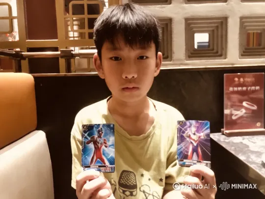 小孩手拿两张奥特曼卡片做出迪迦奥特曼的变身动作（1秒时间左右完成动作）。动作结束后画面恢复到一开始的样子。突然视频的画面抖动，两张奥特曼卡片开始闪闪发光，银河奥特曼和特利迦奥特曼分别从左右两张卡片中飞出来，并以和正常人一样的大小坐在小孩的左右两边和小孩聊天[推出,上升,下摇] by Hailuo AI Video Generator