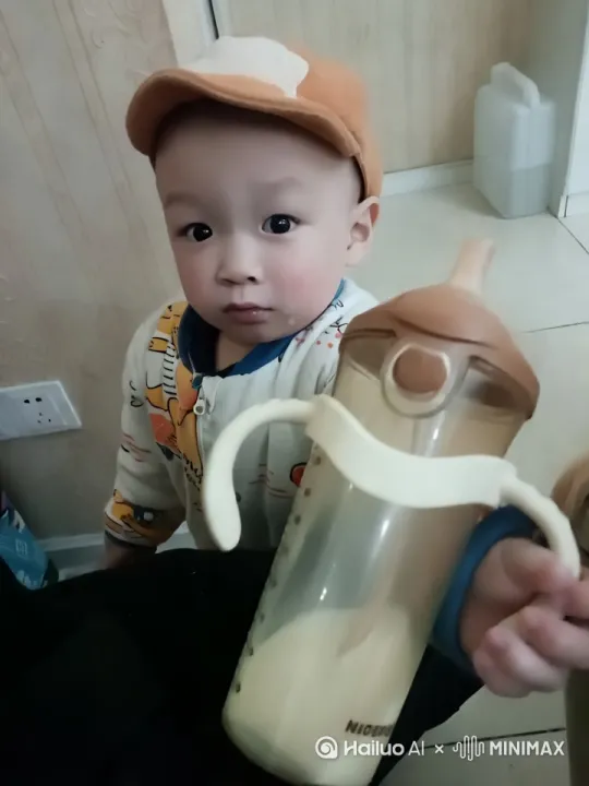 一个二岁萌宝，在喝奶的时候，看到爷爷到来，随手把奶瓶举起来，满脸笑容。 by Hailuo AI Video Generator
