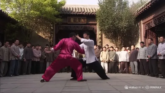 The video depicts an intense martial arts fight scene taking place in an outdoor courtyard, likely part of a traditional Chinese martial arts school (indicated by the sign in the background). Two male martial artists are engaged in combat. One wears a red/pink traditional martial arts uniform, while the other wears a white shirt and dark pants. The fight is fast-paced and dynamic, featuring a series of punches, blocks, parries, and a high-flying kick. An audience of onlookers is visible in the background, watching the fight intently. The style and setting suggest a scene from a classic Hong Kong action or martial arts film. by Hailuo AI Video Generator
