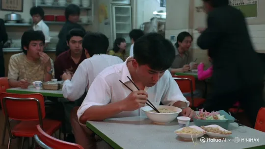 镜头环绕着白衣人旋转：90年代香港的茶餐厅，一个白衣男人在桌上吃面。他背后突然跑来一个黑衣人， 拿刀向他砍来，他迅速灵活闪开躲过后面的那刀，转身把手上的筷子用力扔向黑衣人的脸，一手夺过黑衣人的刀，一条踢开黑衣人。旁边吃饭的人惊叫闪躲。 by Hailuo AI Video Generator