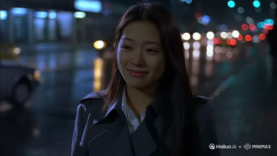 主体：一个亚洲年轻女人，侧身对镜头，瓜子脸，五官美丽，长发，穿着深灰色的风衣，里面是一件白衬衣。表情强装镇定的微笑，逃避镜头一般向远处左右观望，又看向镜头，再也忍不住，低头委屈哭泣，微表情变化，影后级表演。环境：深夜街头，背景虚化的车流和绚烂的街灯，天空下着肉眼可见的小雨。近景，专业定焦镜头[固定镜头]，比例9:16。 by Hailuo AI Video Generator