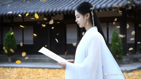 跟随镜头。身着白色汉服裙袍的少女，正侧脸对着镜头，在落叶飘零的院落里，手捧诗卷，低眉读书，缓步而行。 by Hailuo AI Video Generator