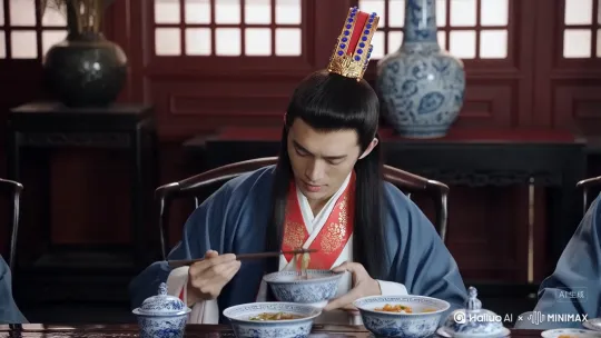 年轻男子、长发束冠、蓝白色汉服、红色镶金花纹领口、宝石发冠（红底配蓝色宝石、金色装饰 ）、长发垂肩。中式传统室内环境、中式古典家具、青花瓷瓶、中式餐具（青花瓷碗盘 ）、中式餐食。手持碗筷用餐、神态专注。 by Hailuo AI Video Generator